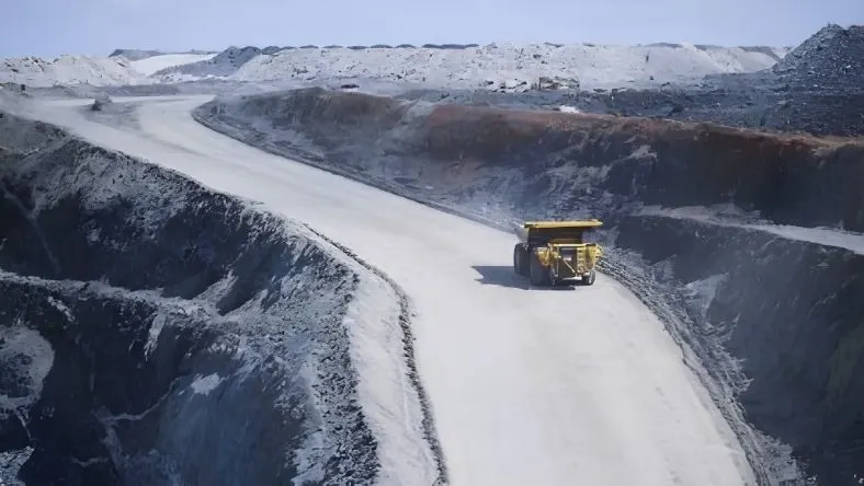 Yellow haul truck on a road in an open-cut mine with grey and white pit walls